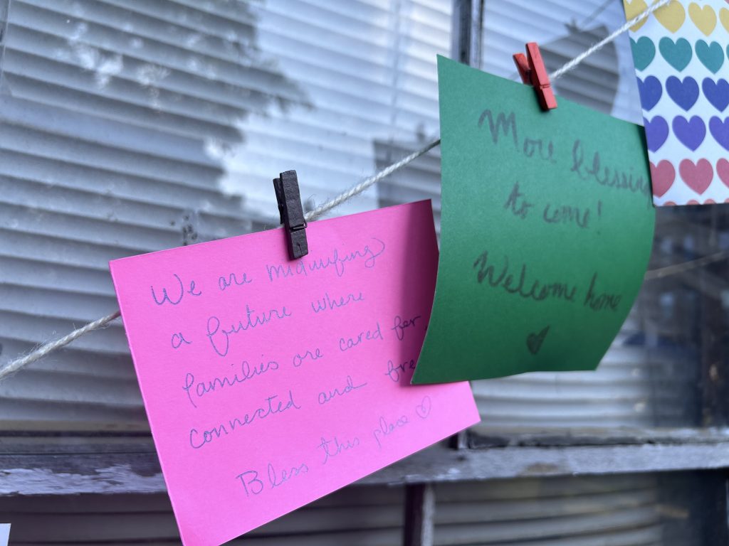 close up photo of two cards with blessings handwritten on them, hung with clothes pins on a string. one card is bright pink and one is dark green.